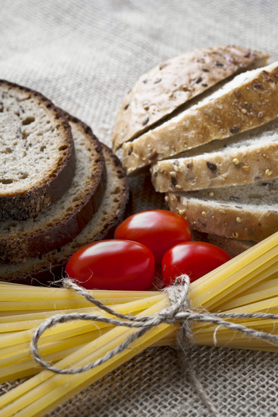 Dry pasta and tomatoes with sliced bread on sack background - Photo, Image