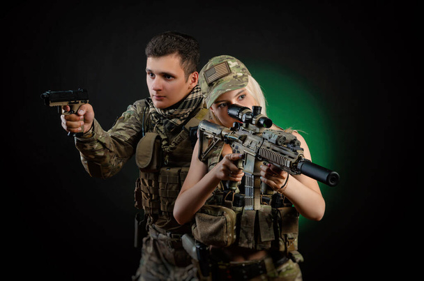 Egy lány és egy fickó katonai overálban, légpuha fegyverrel, sötét háttérrel. - Fotó, kép