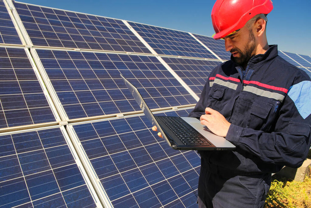 Працівник у червоному шоломі та ноутбуці на сонячній електростанції
 - Фото, зображення