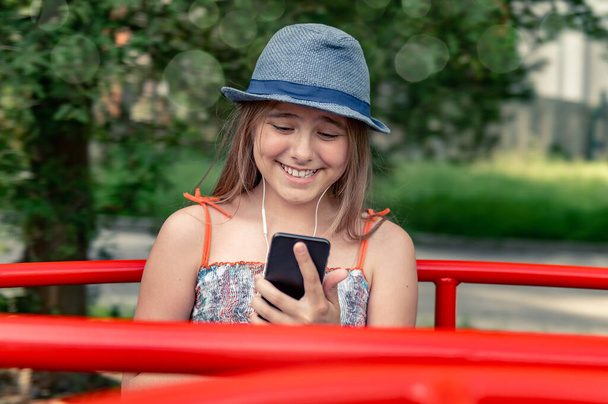 Lonley tienermeisje communiceert in een park op een draaimolen. glimlachende tiener met telefoon - Foto, afbeelding