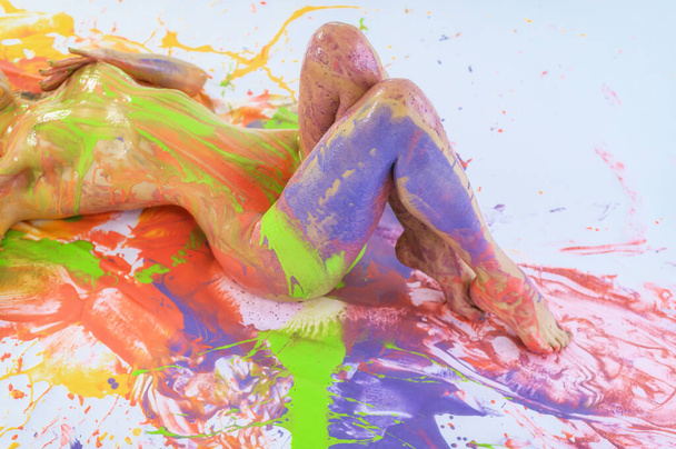Nude woman in stains of paint on a white floor. View from above. Cropped. Color splashes on the skin. Art body painting. - Foto, Imagen