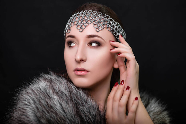 Beauty portrait of a woman with a chain mail bezel on her head and fur on her shoulders. Studio photo on a black background. Model with clear skin, retouch. - Fotoğraf, Görsel