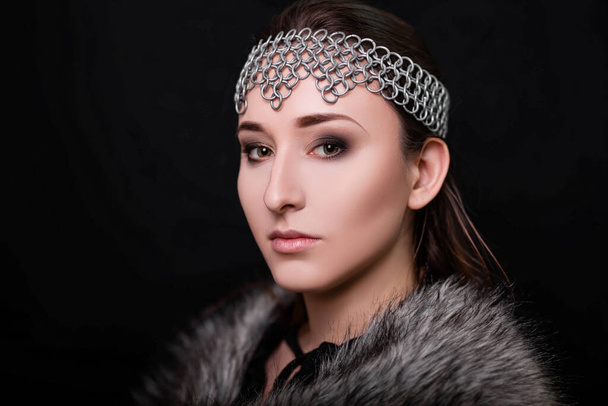 Beauty portrait of a woman with a chain mail bezel on her head and fur on her shoulders. Studio photo on a black background. Model with clear skin, retouch. - Foto, Bild
