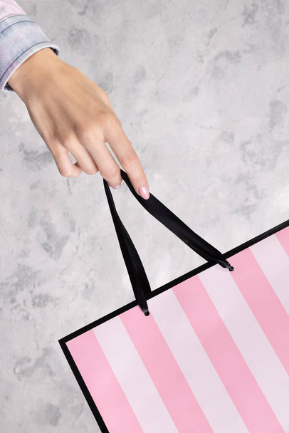 Female hand holding paper shopping bag over gray concrete background. Summer sale concept - Foto, imagen