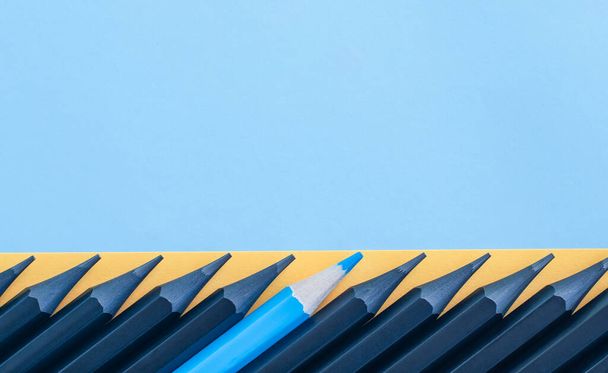 a lot of black pencils in a row, among them one blue - Zdjęcie, obraz