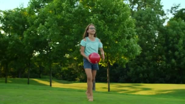 Boldog lány áll a zöld mezőn. Csinos lány kezében labda - Felvétel, videó