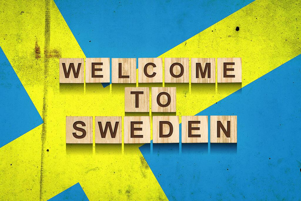スウェーデンへようこそ。スウェーデンの国旗を背景に木製のブロックに刻まれている。旅行. - 写真・画像