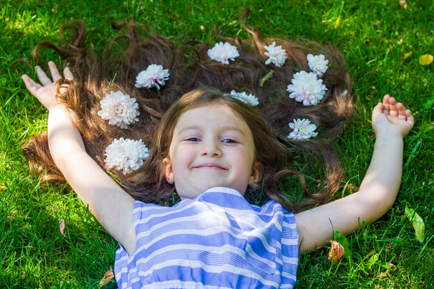glückliches kleines Mädchen, hübsches kleines Mädchen, das im Gras mit Blumen liegt - Foto, Bild