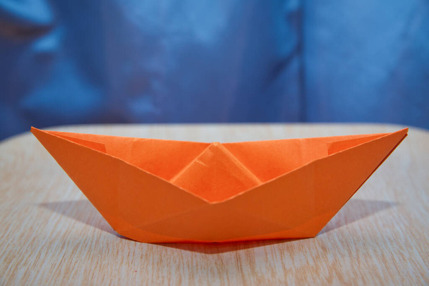 Origami papírhajó. Vezetői koncepció narancssárga papírhajóval a fa között. Narancs papírhajó fa és kék háttér . - Fotó, kép