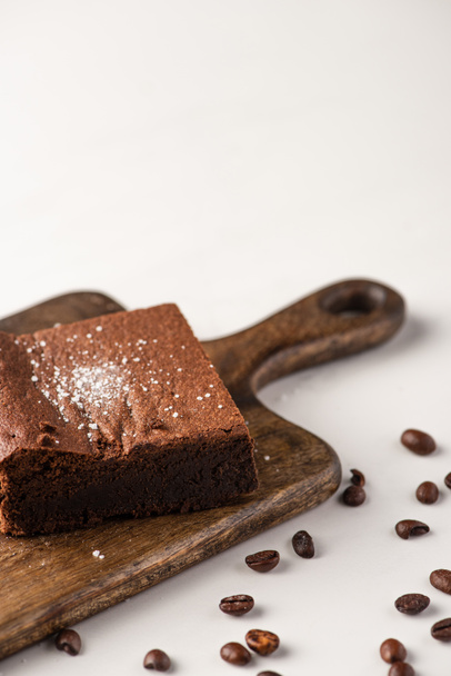 delicious brownie piece on wooden cutting board with coffee beans on white background - Foto, Imagen