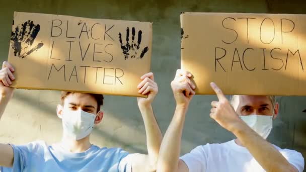 Двоє чоловіків у масці з картонним плакатом у руках з написом STOP RACISM. Одне протестування.
. - Кадри, відео