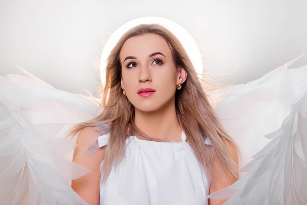 Angel in a white dress with large white wings behind his back and a halo above his head. Portrait of an attractive girl in a fantasy look. - Photo, image