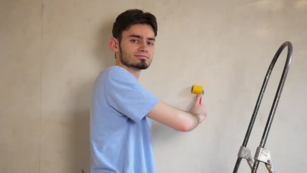 Egy kék pólós fickó felirat nélkül áll a lépcső mellett javításra. Javítás a házban. Falfestés - Felvétel, videó
