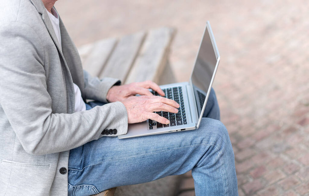 Бизнесмен сидит на скамейке и пользуется ноутбуком  - Фото, изображение