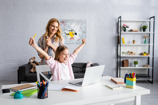 Smiling woman standing near happy child showing yeah gesture during online education  - Foto, Imagen