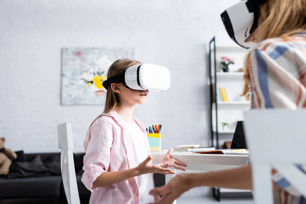 Selective focus of kid using vr headset near mother and stationery on table  - 写真・画像