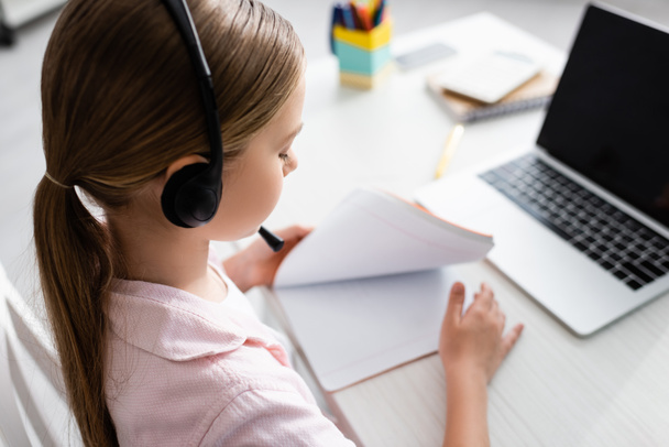 Selective focus of child in headset holding copy book during electronic learning  - Foto, Bild