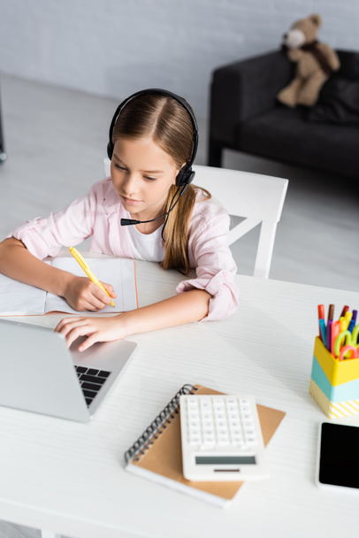 Enfoque selectivo del niño escribiendo en el portátil mientras usa auriculares y computadora portátil en la mesa
  - Foto, Imagen