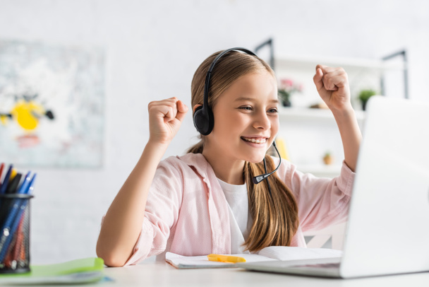 Selektywne skupienie się na uśmiechniętym dziecku w zestawie słuchawkowym pokazującym gest tak podczas edukacji online w domu  - Zdjęcie, obraz