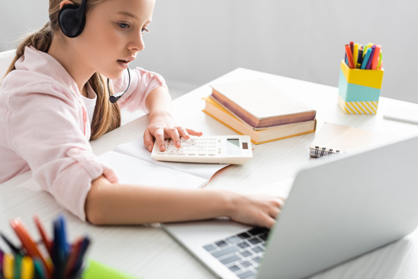 Enfoque selectivo del niño con auriculares usando computadora portátil y calculadora durante la educación en línea
  - Foto, Imagen