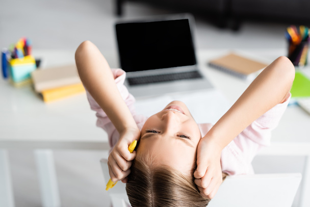 Pohled shora na unavené dítě držící pero během online vzdělávání  - Fotografie, Obrázek
