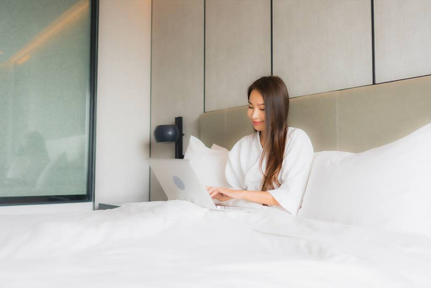 Портрет красива молода азіатка використовує ноутбук або комп'ютер в інтер'єрі спальні
 - Фото, зображення