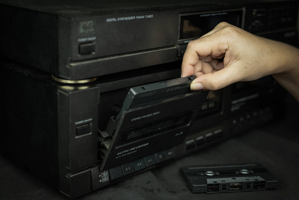 Женщина рука вставляет компактную кассетную ленту в старый плеер аудио ретро-технологии
 - Фото, изображение
