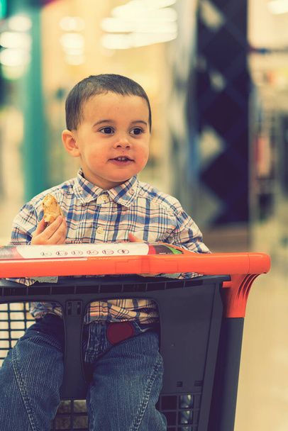 Gömlekli mutlu bir çocuk alışveriş merkezinde bir tramvayda oturur ve ekmek yer. ses tonlu. - Fotoğraf, Görsel