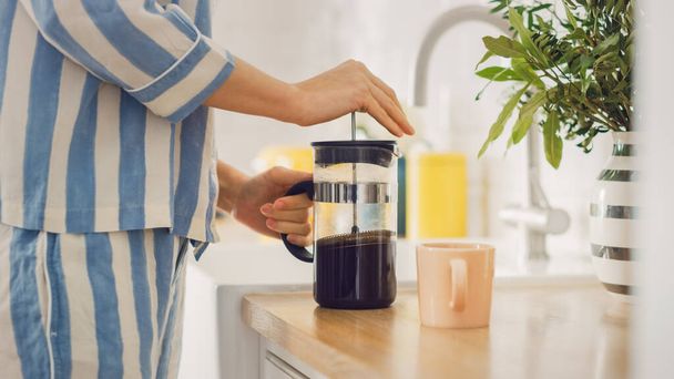 Authentic Concept of a Female in a Kitchen Room at Home Preparing a Cup of Freshly Brewed Coffee from a French Press. Girl in Pyjamas with Healthy Creative Lifestyle Relaxes at Home in the Morning. - 写真・画像