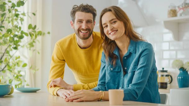 Happy Handsome Young Man in Yellow Jumper and Beautiful Joyful Girl in Jeans Shirt are Posing Together as a Couple. They Sit and Smile in a Sunny Modern Home Kitchen with Healthy Lifestyle Vibes. - Foto, immagini