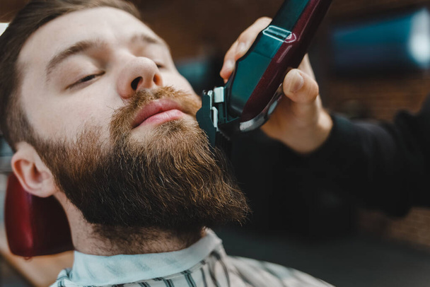 Barber master cuts a beard to a client close-up - Fotografie, Obrázek