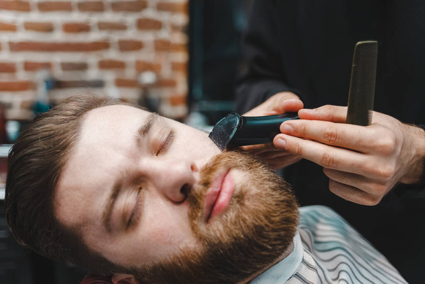 Peluquería Master corta la barba del cliente con trimmer eléctrico
 - Foto, imagen