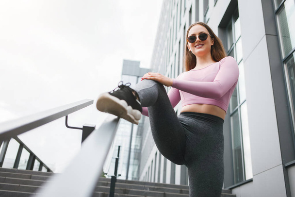 Smiling fitness woman doing workout. Girl is stretched on the stairs - Foto, immagini