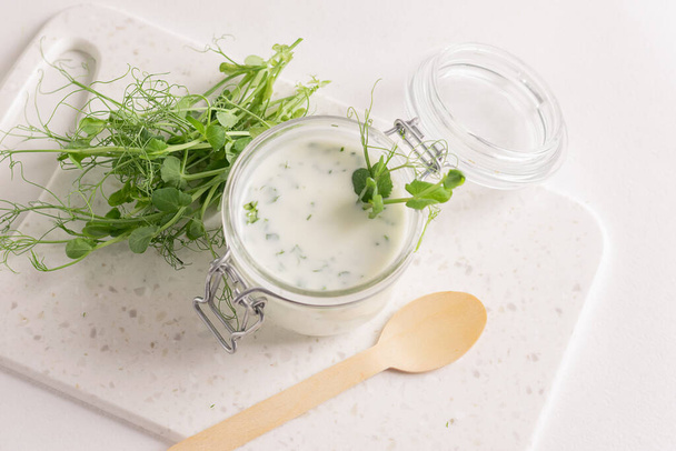 白いキッチンテーブルの上に新鮮なマイクログラスもやしの緑を追加したサワーミルク製品ドリンク. - 写真・画像