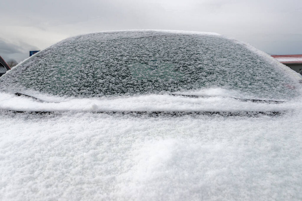 Un primer plano de un coche con un parabrisas cubierto de nieve y capucha. El coche no es identificable. Cielo nublado arriba
. - Foto, imagen