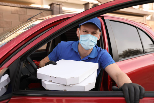 Mensajero en máscara protectora y guantes con cajas de pizza saliendo del coche al aire libre. Servicio de entrega de alimentos durante la cuarentena del coronavirus
 - Foto, imagen