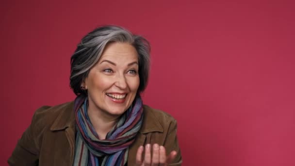 Funny mature woman laughs gesturing by hand and looking at side. Creative aged lady posing in studio on pink background. Prores 422 - Imágenes, Vídeo