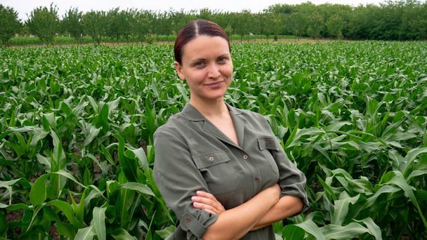 トウモロコシ畑で腕を組んで満足した女性農家。農業ビジネスにおける女性. - 写真・画像
