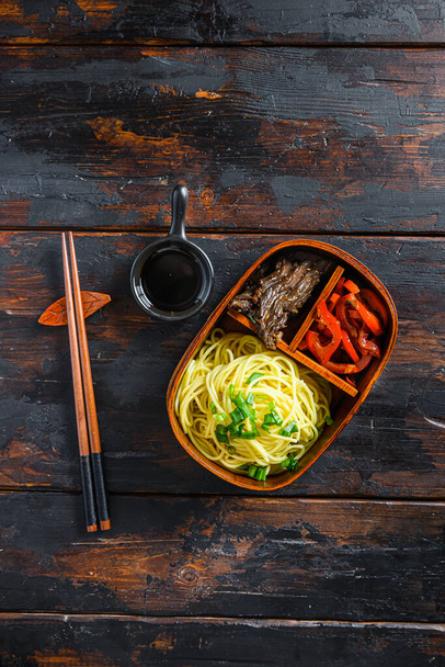 Zelfgemaakte Bento-pakket lunch, gegrild rundvlees en noedels met ingrediënten bovenaanzicht donker houten tafel - Foto, afbeelding
