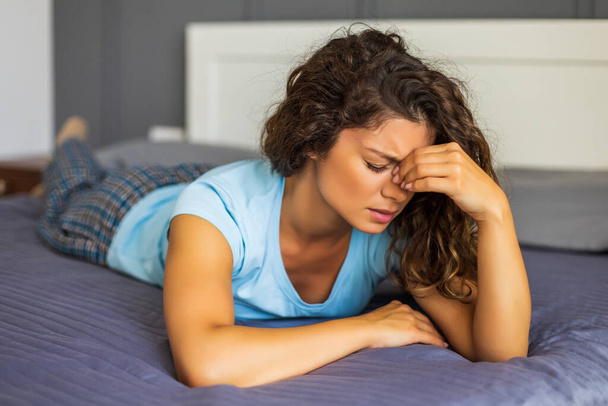Worried woman having strong headache while lying on her bed in bedroom. - Photo, image