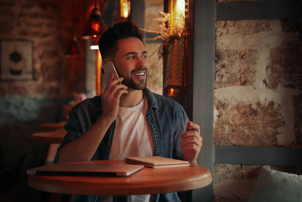 Young blogger talking on phone at table in cafe - Photo, image