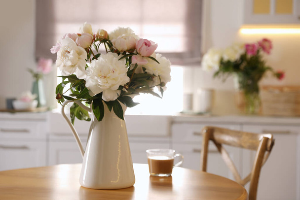 Beautiful peonies and cup of coffee on wooden table in kitchen - Foto, afbeelding