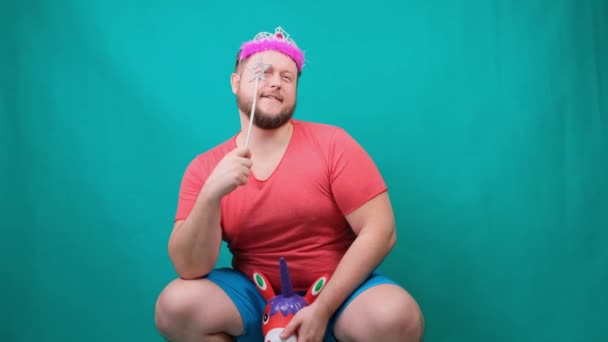 cute bearded freaky man in a pink T-shirt with a diadem on his head dreams of riding a unicorn with a magic wand in his hand. A funny wizard joke to make and fulfill a wish - Footage, Video