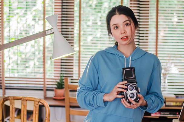 Stylish vintage female photographer  holding her old  twin lens camera to her chest as she composes her image with a serious expression - Photo, Image