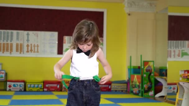 Een jongen met lang haar kleedt alleen groene bretels aan en loopt rond. - Video