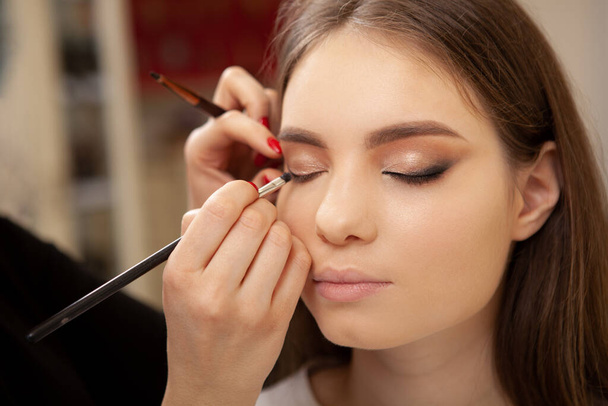 Cropped shot of unrecognizable makeup artist working at beauty salon, blending eyeshadow on eyelids of a female client - Foto, Bild