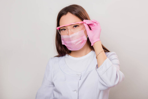 Portrait of a woman in a white coat, mask and with hands in gloves holds on to the glasses. Photo on a white background. - Foto, immagini