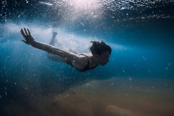 Mergulho de mulher sem prancha sob onda oceânica. Pato subaquático mergulhar sob onda e fundo arenoso
 - Foto, Imagem