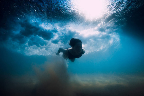 Een vrouw duikt zonder surfplank onder de oceaangolf. Onderwater eendenduik onder golf- en zandbodem - Foto, afbeelding