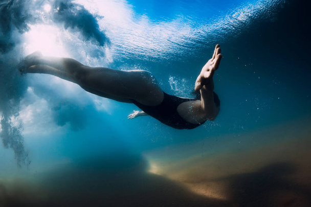 Nainen sukeltaa ilman surffilautaa meren aallon alla. Vedenalainen ankka sukeltaa aallon alla ja hiekkainen pohja - Valokuva, kuva